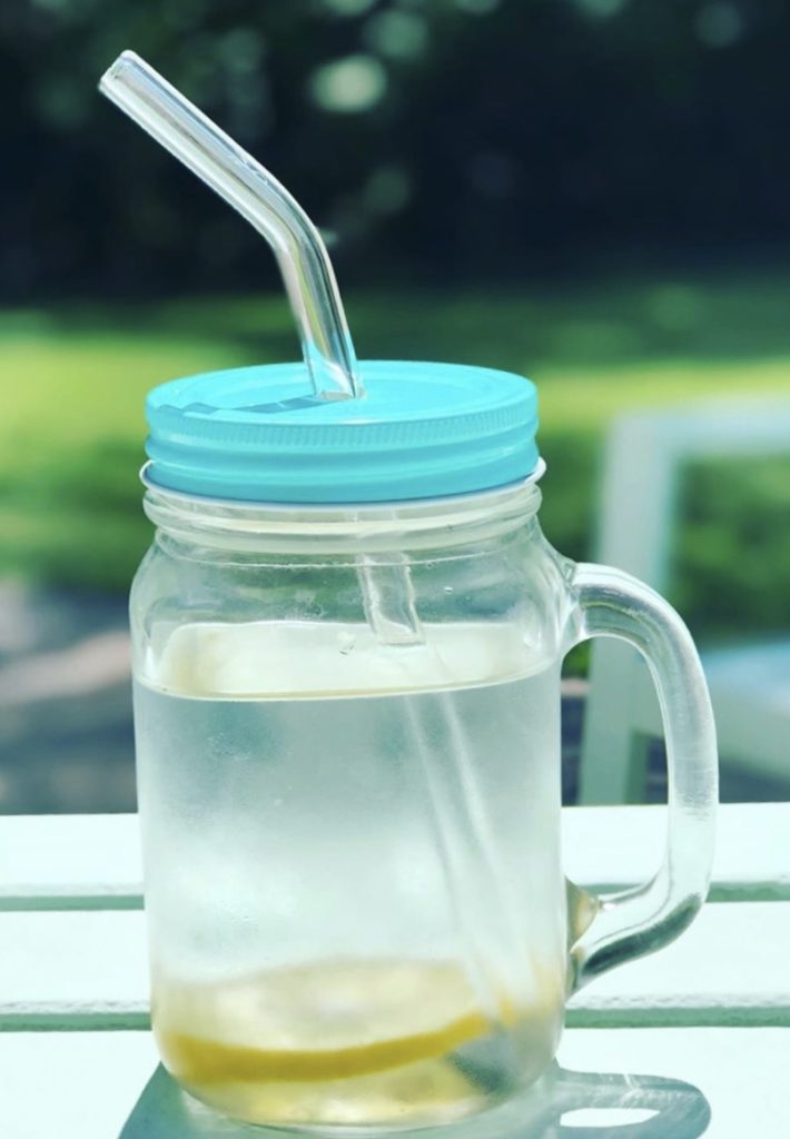 Glass jar with blue lid and metal straw filled with water and a lemon slice