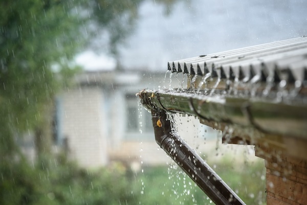 Rain pouring over a house gutter in Charlotte, illustrating the increased rainfall as a consequence of climate change, impacting home insurance rates.
